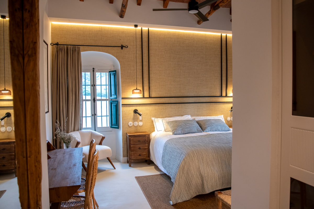 Elegante habitación con cama doble, butaca, escritorio y luz natural