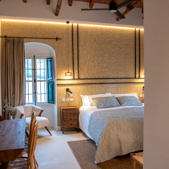 Elegante habitación con cama doble, butaca, escritorio y luz natural