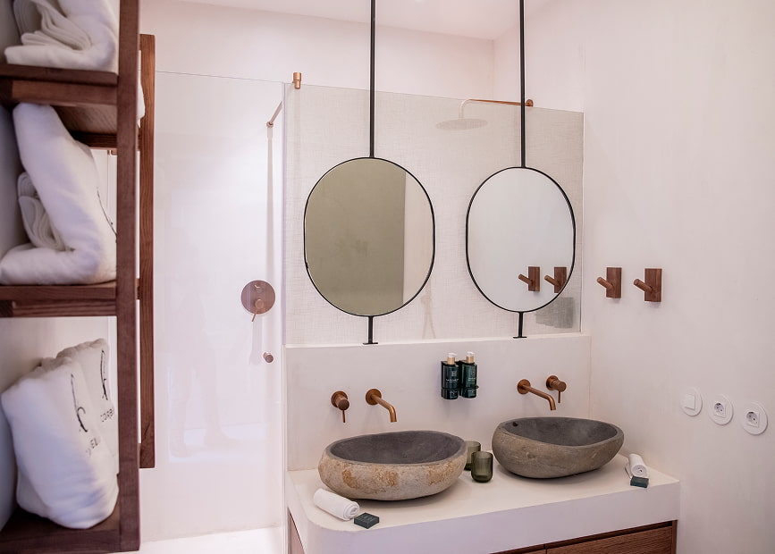 Washbasin on a designer countertop, next to a shelf with towels embroidered with the Hotel Corbella logo.